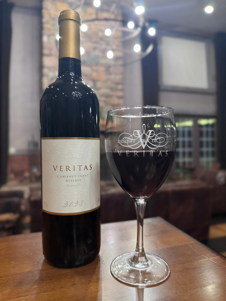 Bottle of Veritas Cabernet Franc Reserve 2023 from the Monticello AVA, with a glass of red wine to the right of it, inside the Veritas tasting room. 