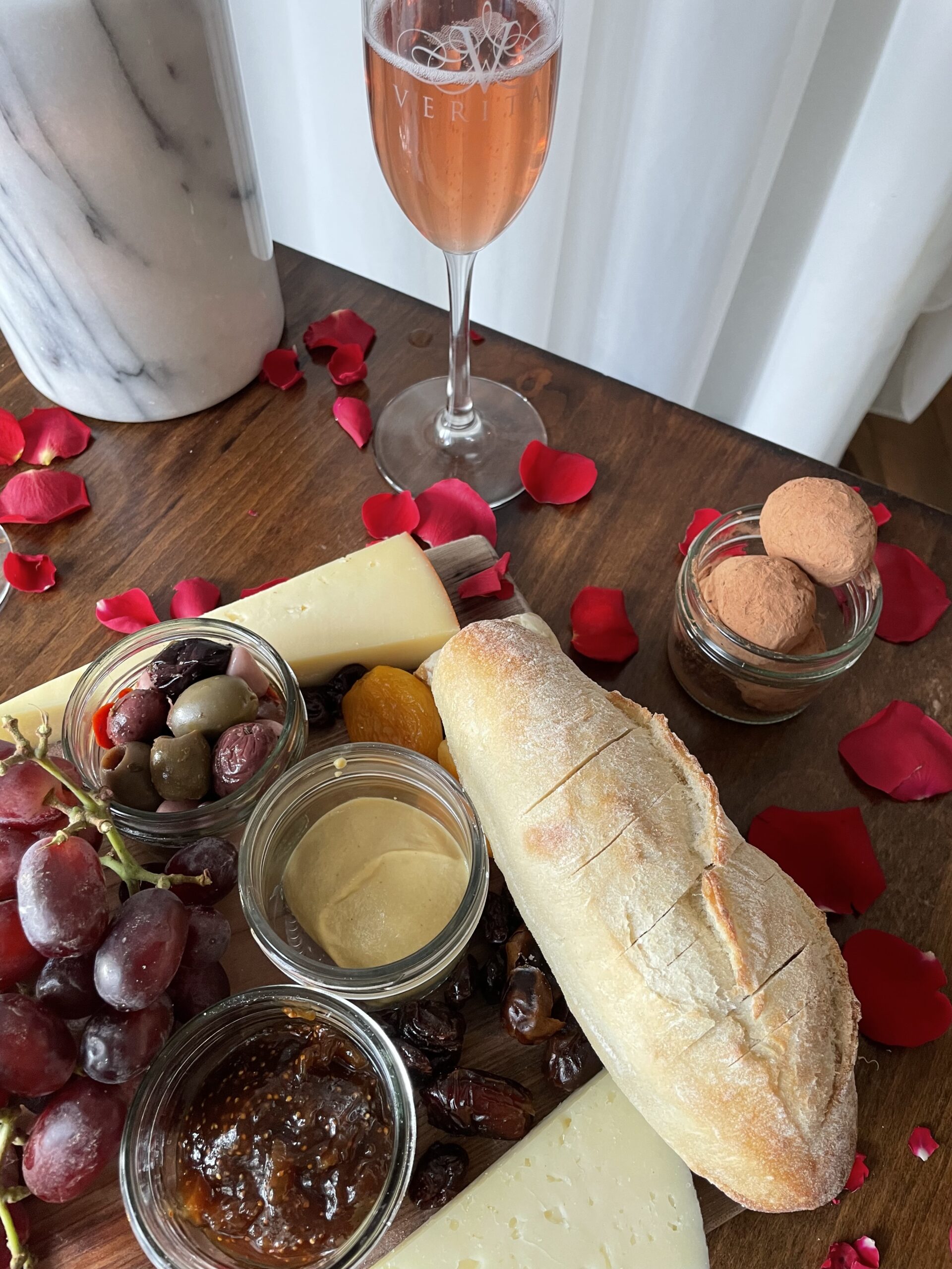 Glass of Veritas Sparkling Rosé, part of a charcuterie board, and small jar of chocolate truffles.