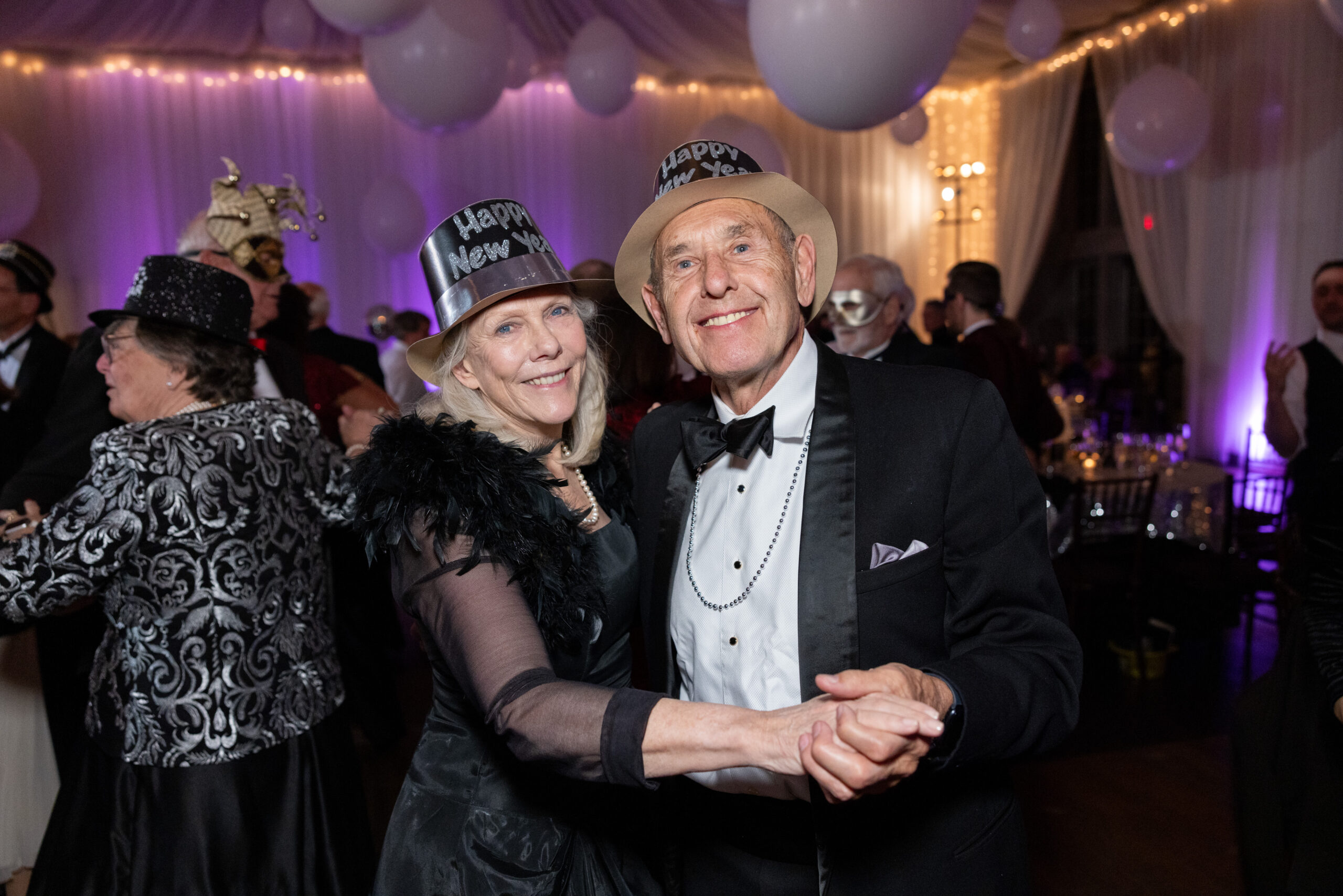Patricia and Andrew Hodson dancing at the Veritas New Year's Eve Masked Ball on December 31, 2023 with decor and people in background. Photo taken by Aaron Watson.
