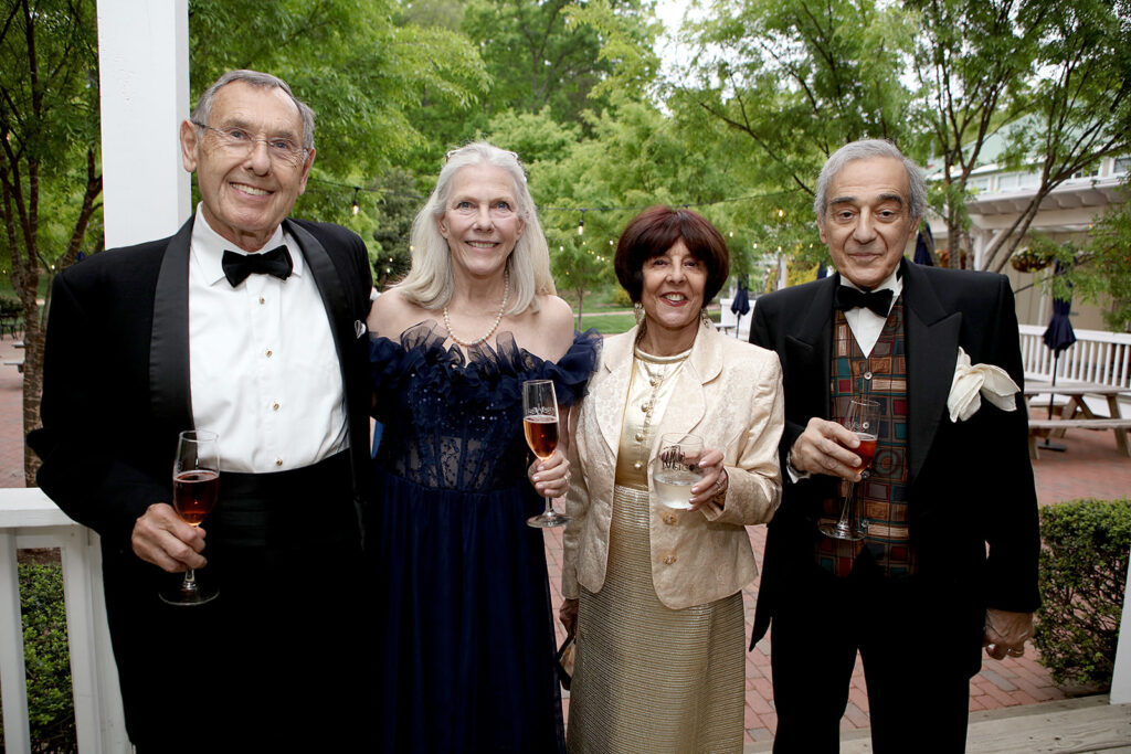 Photo of two men and two women standing outside the Veritas Tasting Room, dressed in evening attire, each holding a glass of wine or water. 