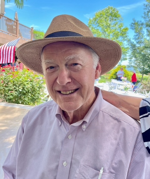 Photo of a man in a hat with a pinstripe shirt sitting outside. 