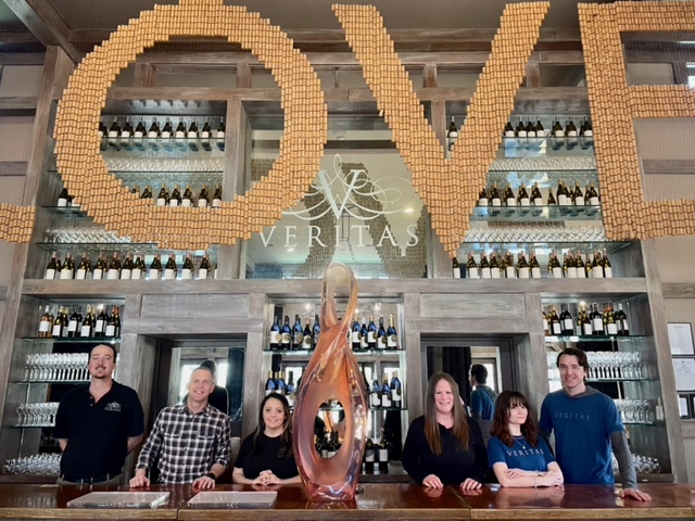 Veritas team members stand behind the bar in the Tasting Room under the infamous Love cork sign. 