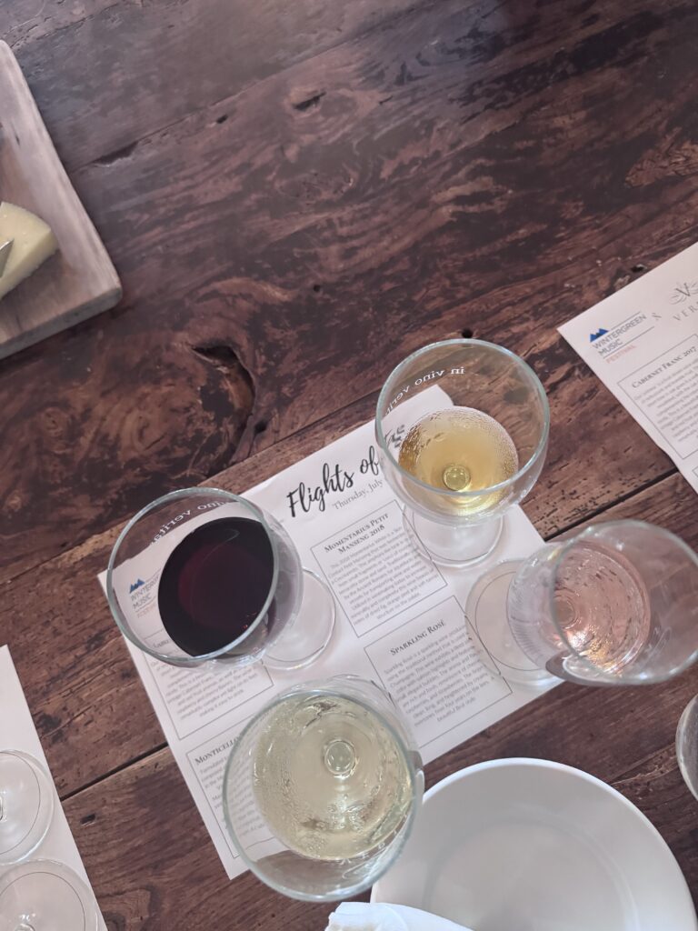 A flight of four wines: one red, two whites and one rose, sit on a table. 