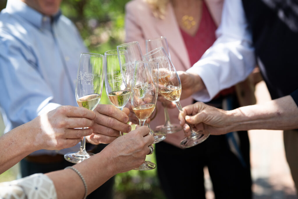A group of people cheers with Veritas sparkling wine glasses, celebrating new ownership. 